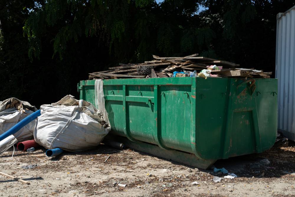 A green dumpster filled with a large pile of wooden debris, showcasing various sizes and shapes of wood materials A green dumpster filled with a large pile of wooden debris, showcasing various sizes and shapes of wood materials